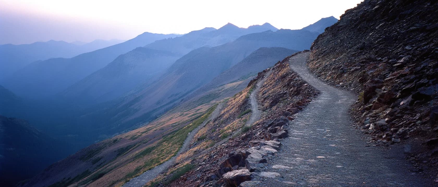 A trail cut into a steep scree slope, winding up toward a high pass