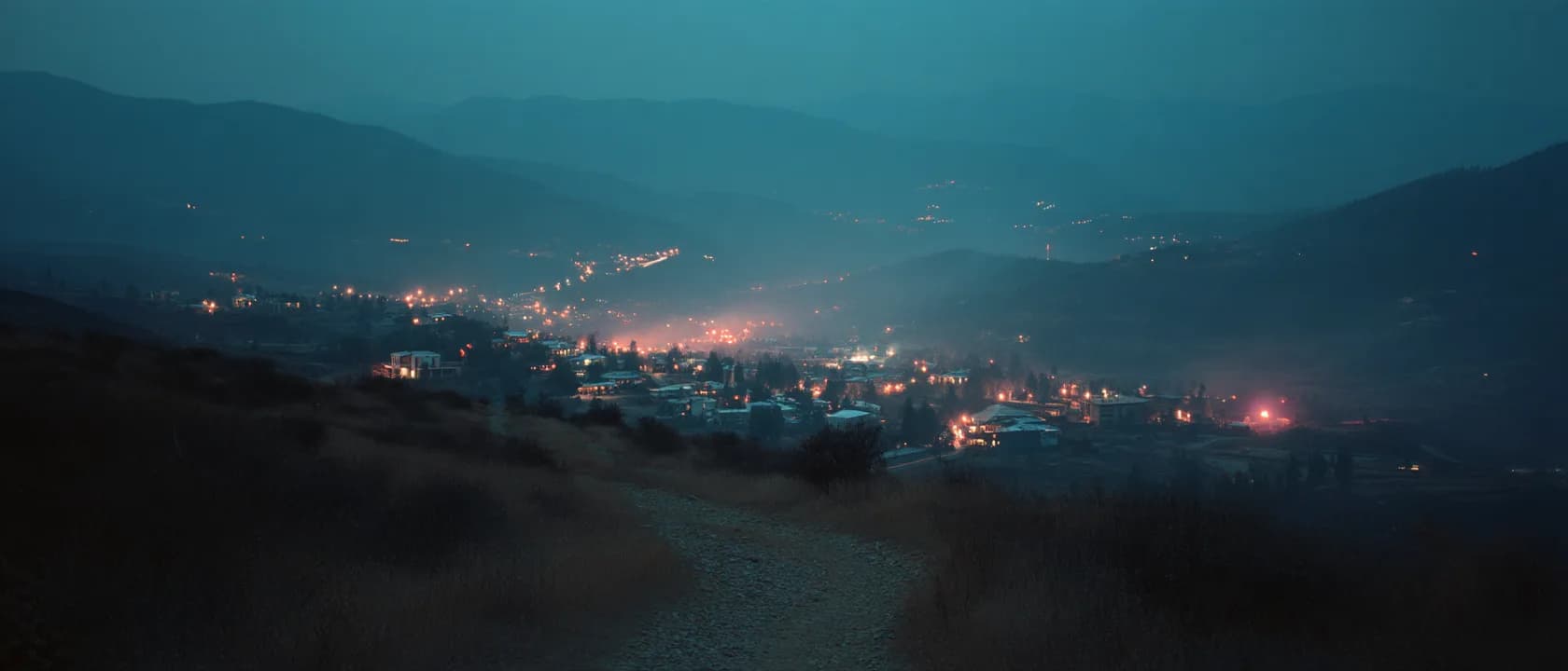A small mountain town at dusk, lit windows below the dark peaks