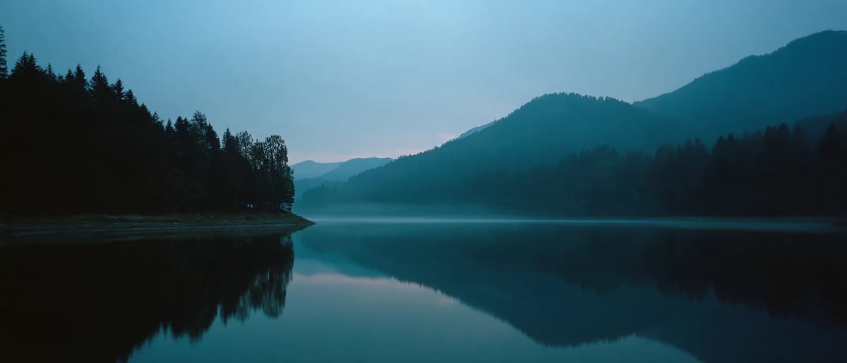 A still mountain lake at dusk mirroring the dark ridges around it